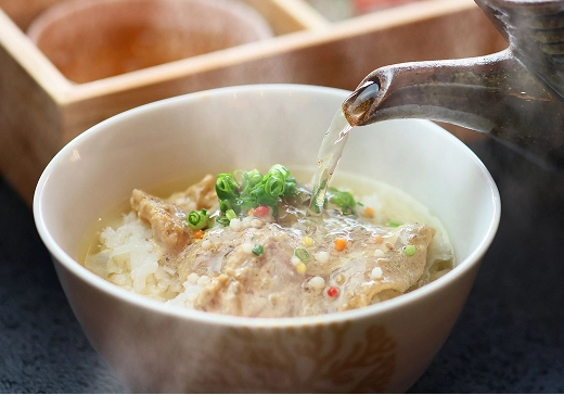 湯気の立つお椀に入ったご飯の上に、熱い出汁を注いでいます。