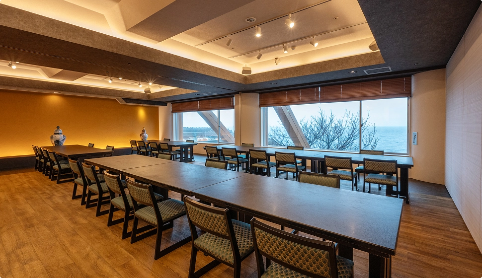 海が見える窓際に長いテーブルと椅子が整然と並べられています。