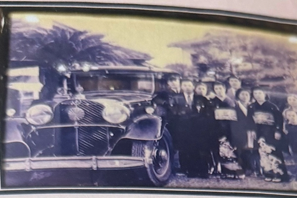 クラシックカーの横に正装した男女の集団が並んで立っています。