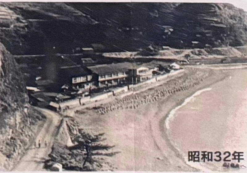 昭和32年頃の海岸沿いに並ぶ古い建物と未舗装の道が写っています。