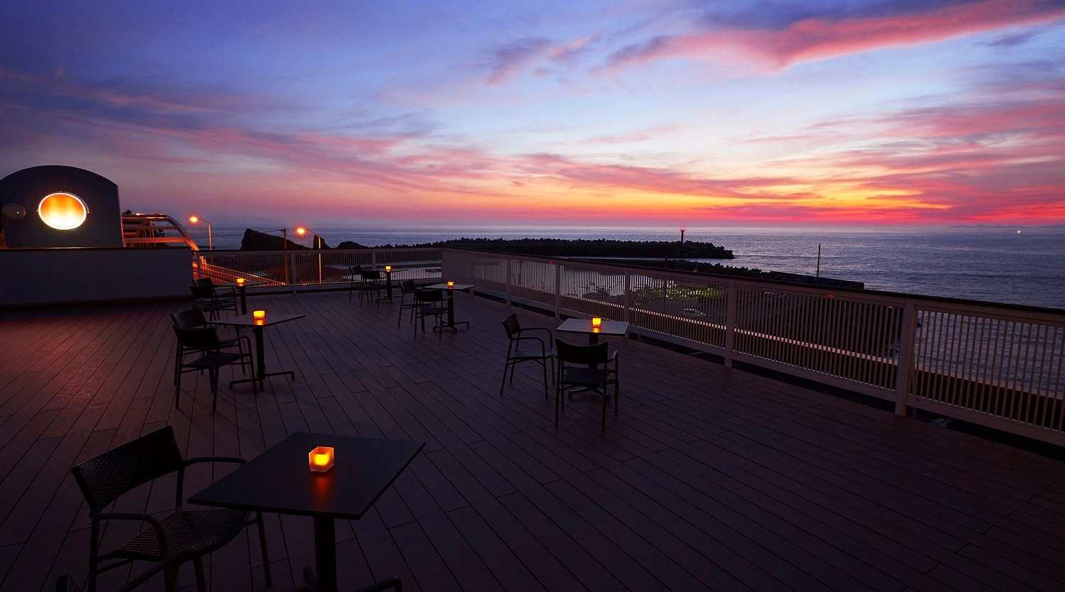 夕暮れ時の海辺にあるテラス席には、テーブルの上に小さな明かりが灯っています。
