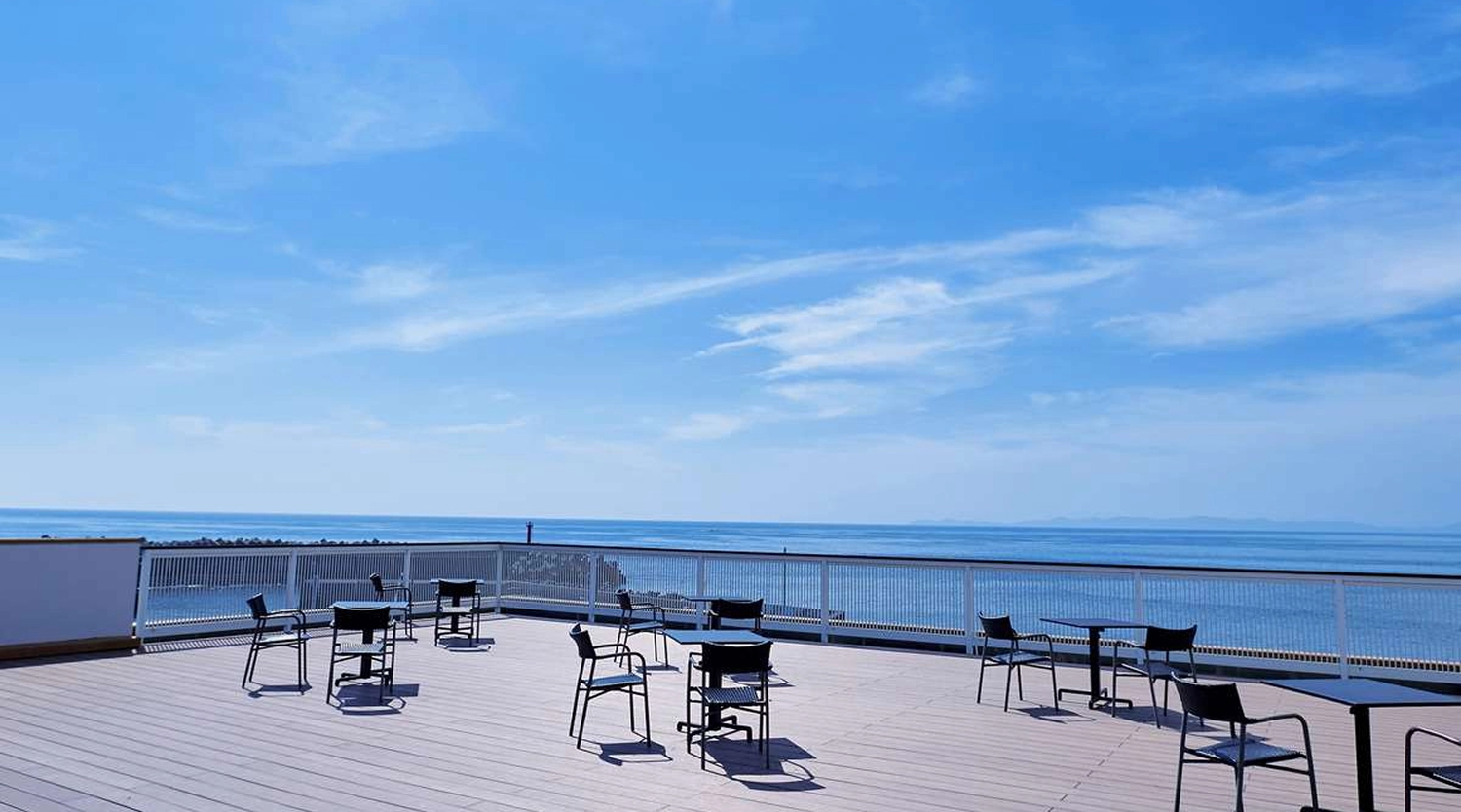 青い空と海が見渡せるウッドデッキのテラス席に、テーブルと椅子が並んでいます。