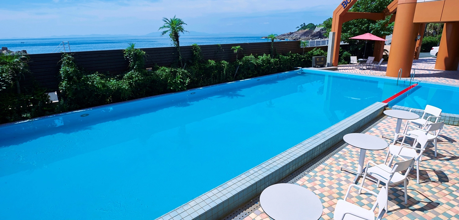 青い海が見えるリゾートホテルの屋外プールサイドに、テーブルと椅子が並んでいます。