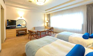 ツインベッドやソファが置かれた明るく清潔感のあるホテルの客室です。