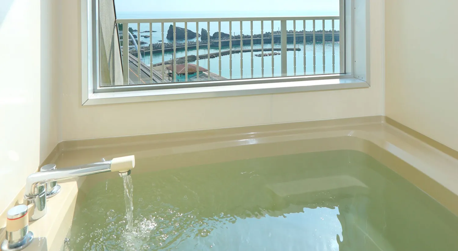 窓から海が見える浴室の浴槽に、お湯が勢いよく注がれています。