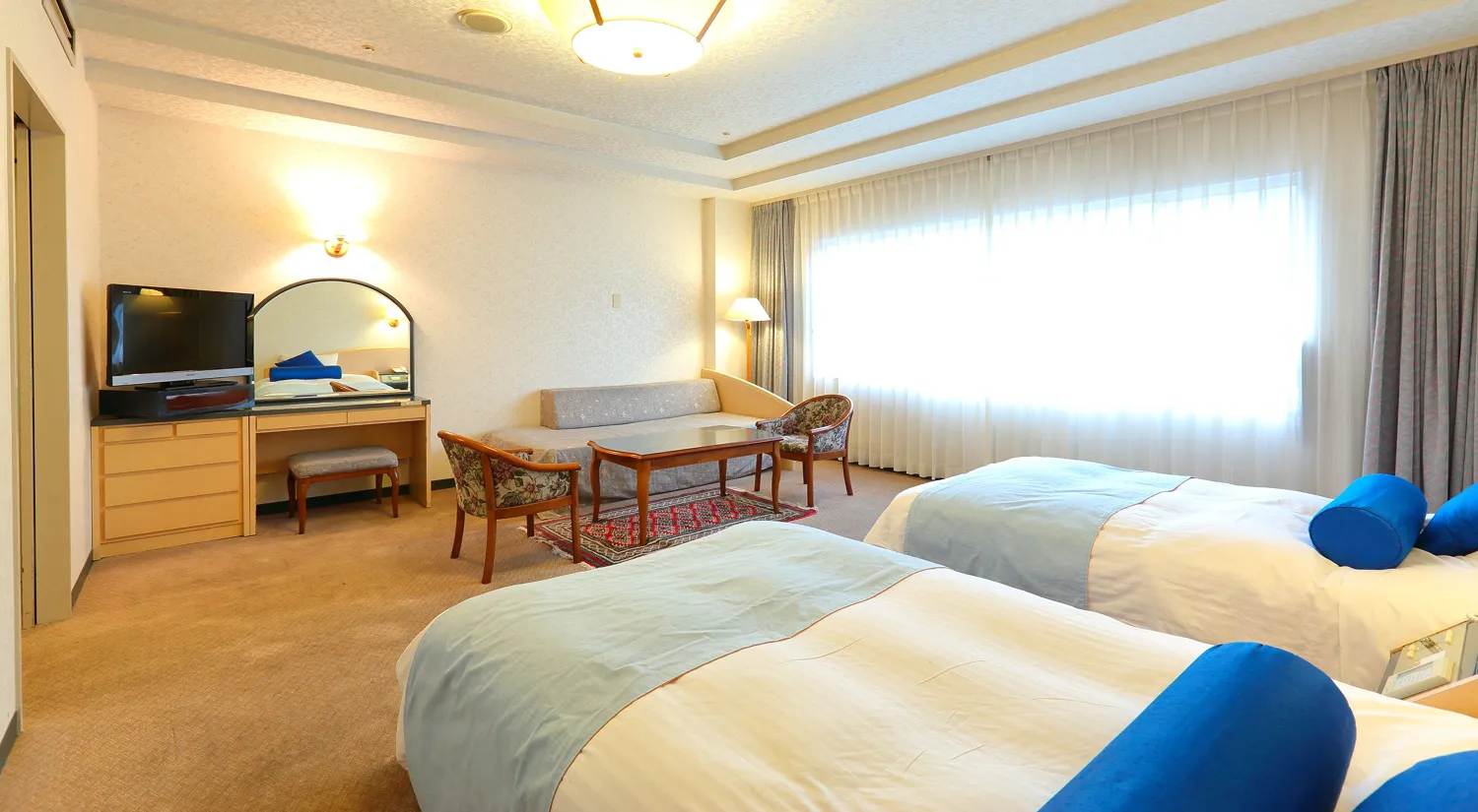 ツインベッドとソファが配置された明るく広々としたホテルの客室です。