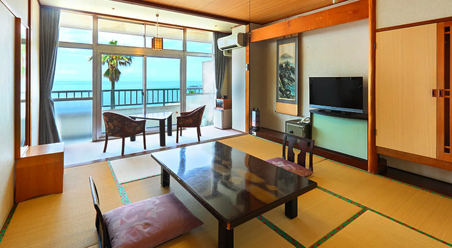 海が見える窓辺にテーブルセットが置かれた、落ち着いた雰囲気の和室です。