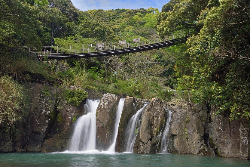 緑豊かな森の中にある滝の上には、木々の間を繋ぐ吊り橋が架かっています。